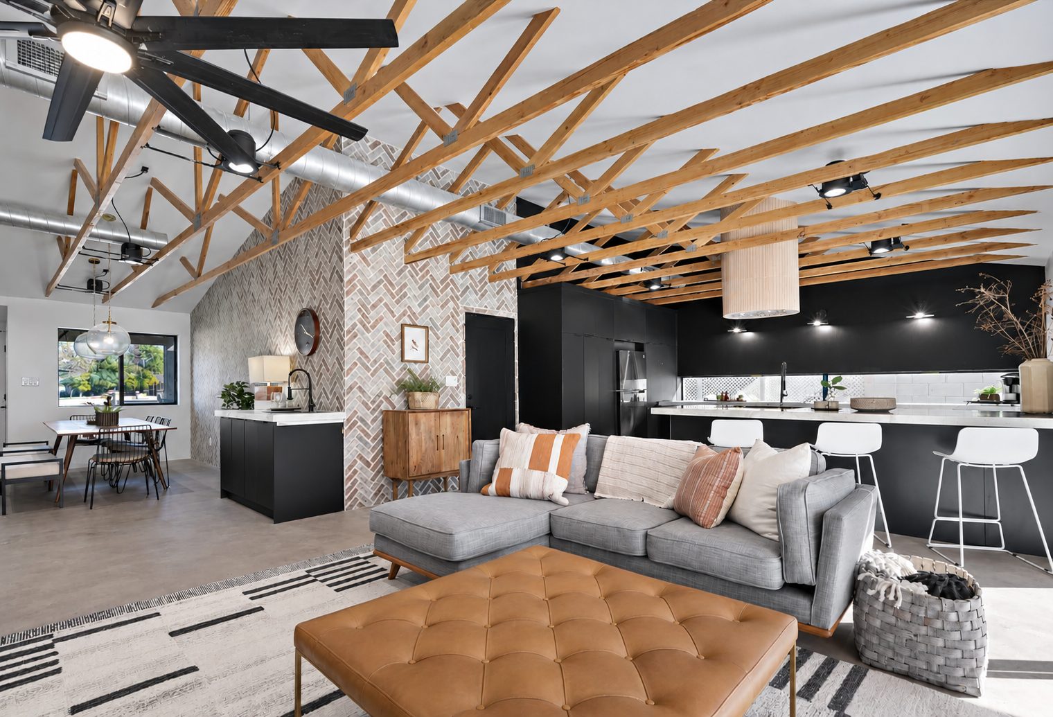 Great room with exposed wood trusses and a herringbone accent wall by Western Desert Construction